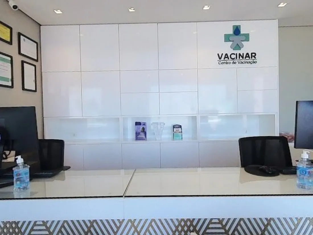 Recepção da Vacinar, com balcão branco e a marca na parede